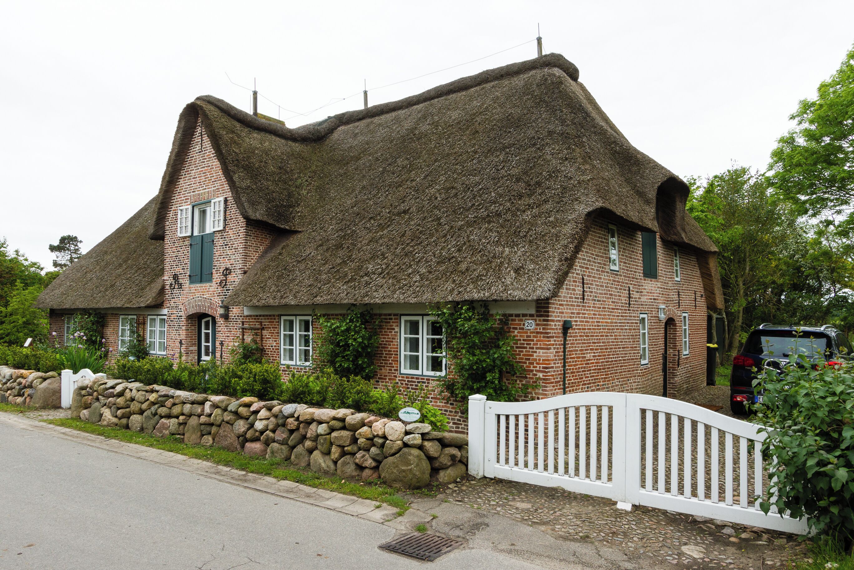 A traditional thatched-roof house with a stone wall and a white picket fence.