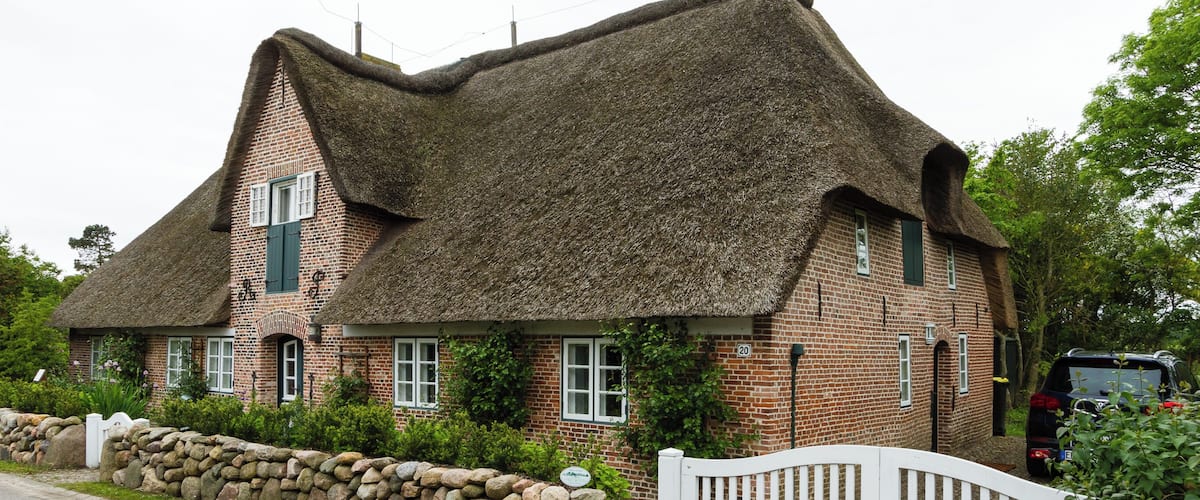 A traditional thatched-roof house with a stone wall and a white picket fence.