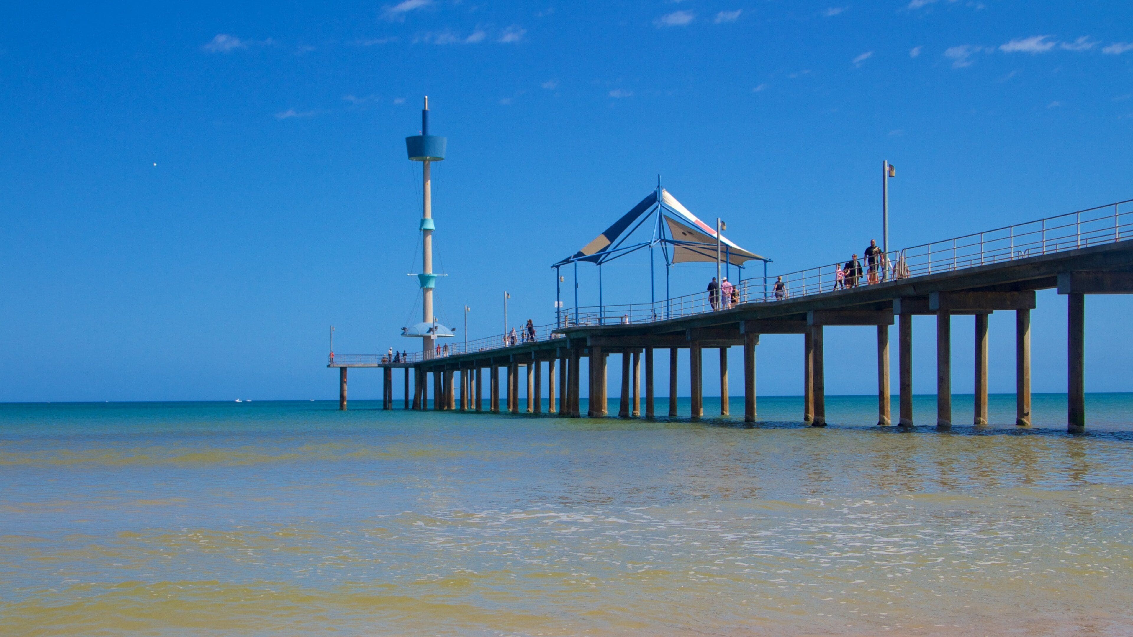 A pier extending into the ocean with a lighthouse and a covered area.