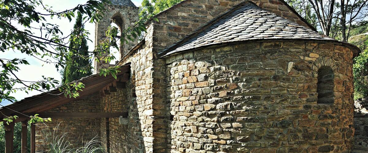 A stone building with a tiled roof, surrounded by trees and a stone pathway.
