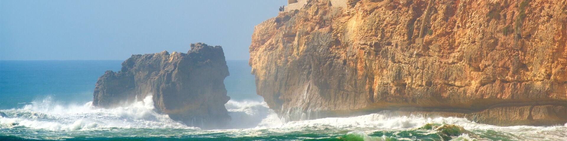 Acantilado costero con un faro y un promontorio rocoso en el mar.