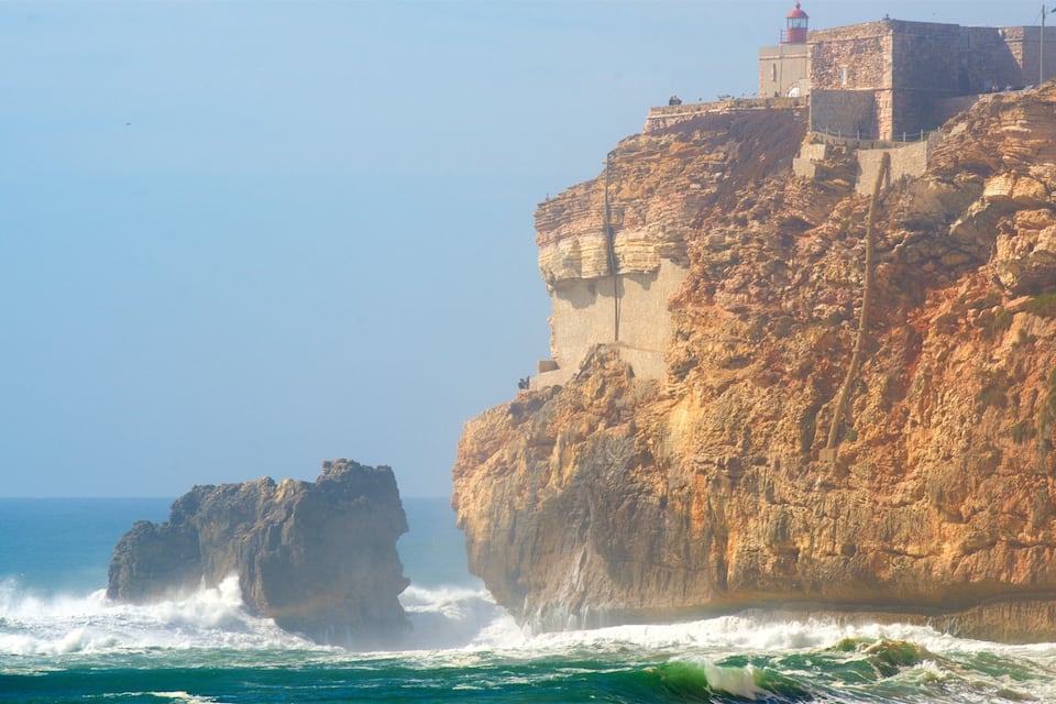 Acantilado costero con un faro y un promontorio rocoso en el mar.