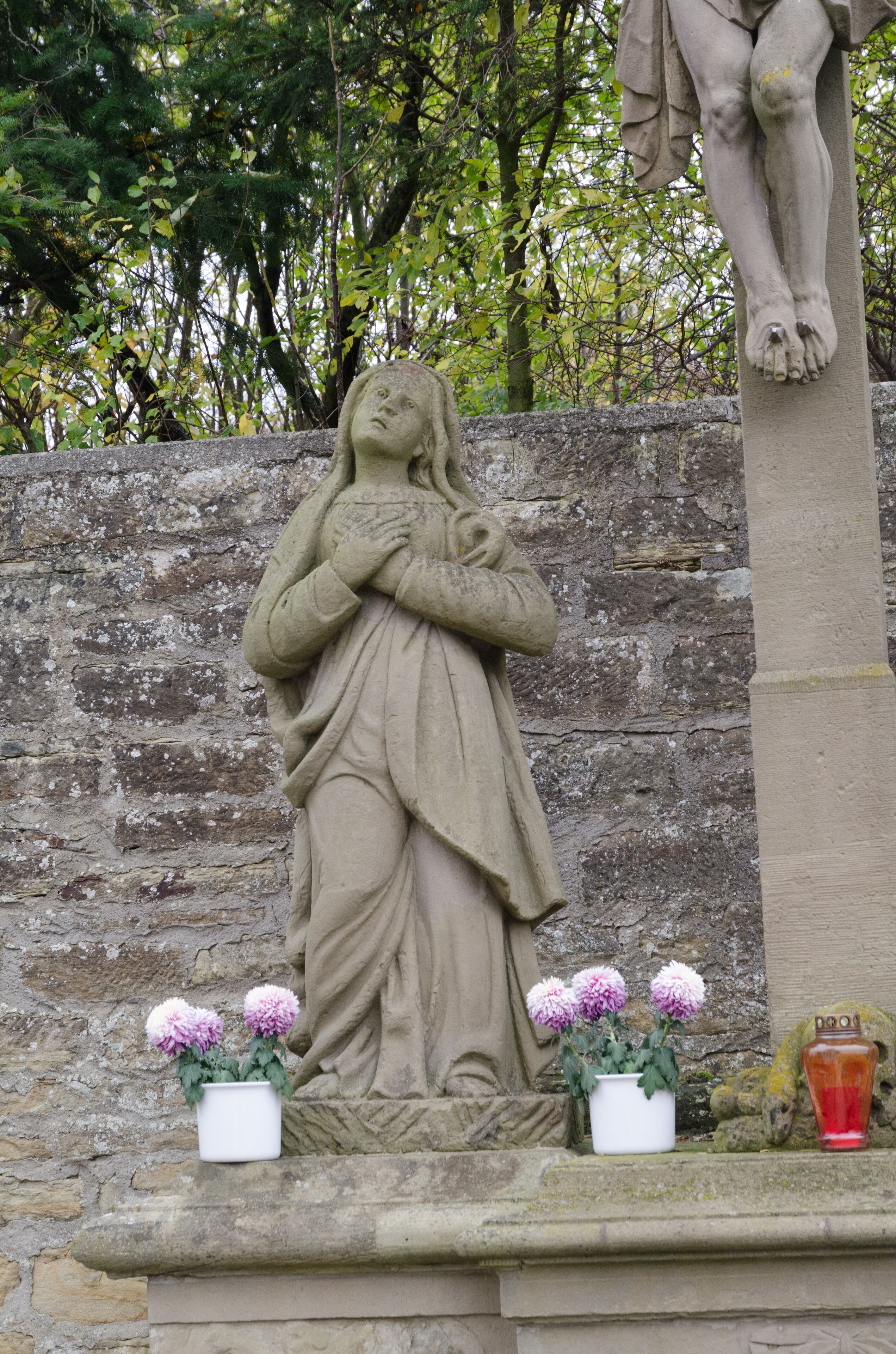 A stone statue of a woman holding a child, with two potted flowers in front.