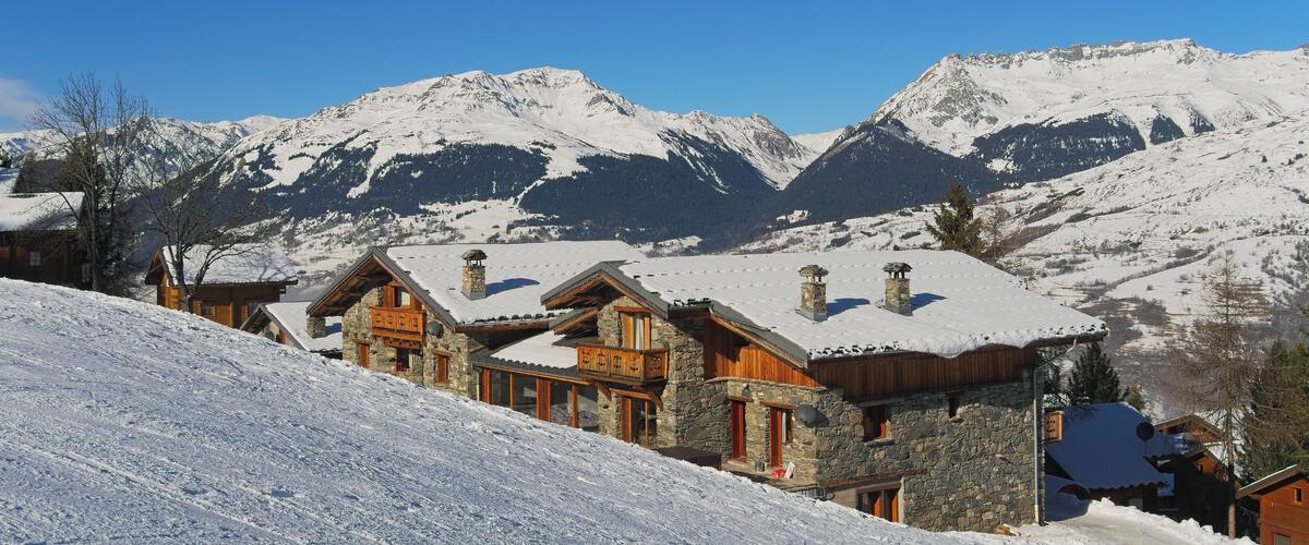 A snow-covered mountain village with wooden houses and a clear blue sky.