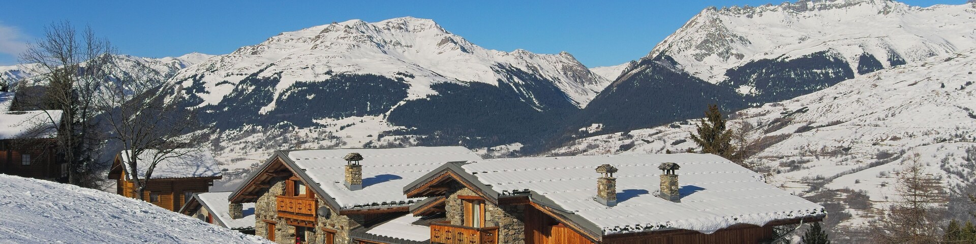 A snow-covered mountain village with wooden houses and a clear blue sky.