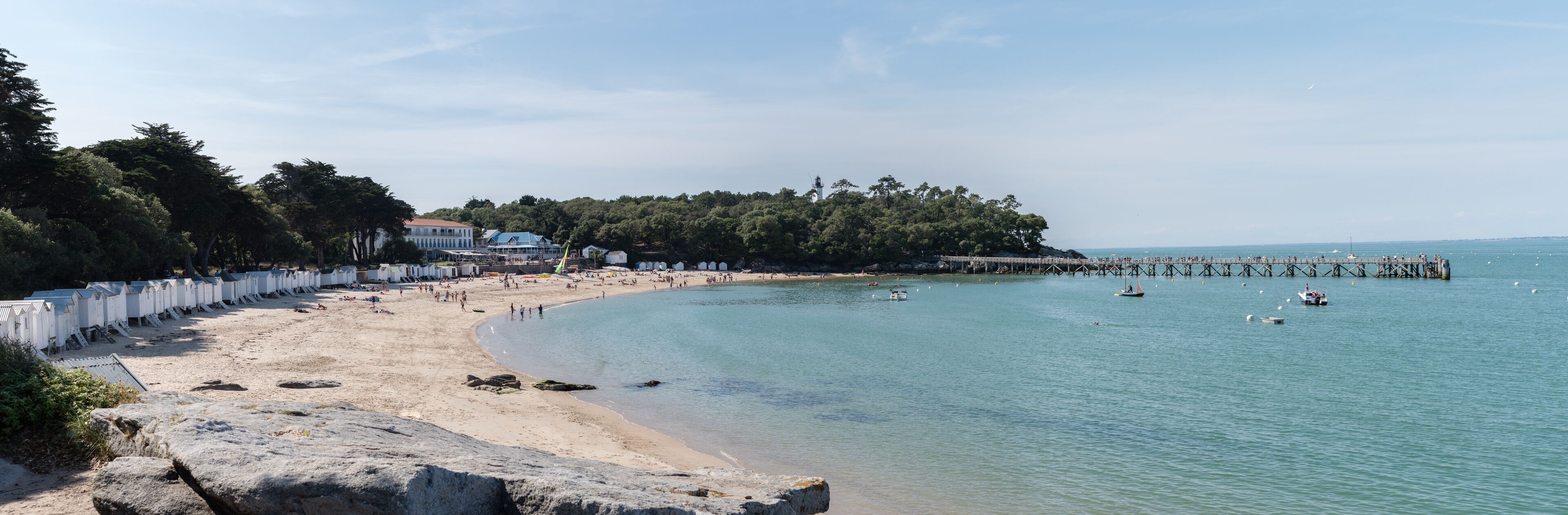 A beach with a pier extending into the water, surrounded by trees and a few buildings.