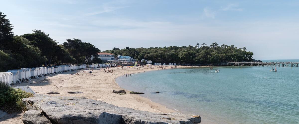 A beach with a pier extending into the water, surrounded by trees and a few buildings.