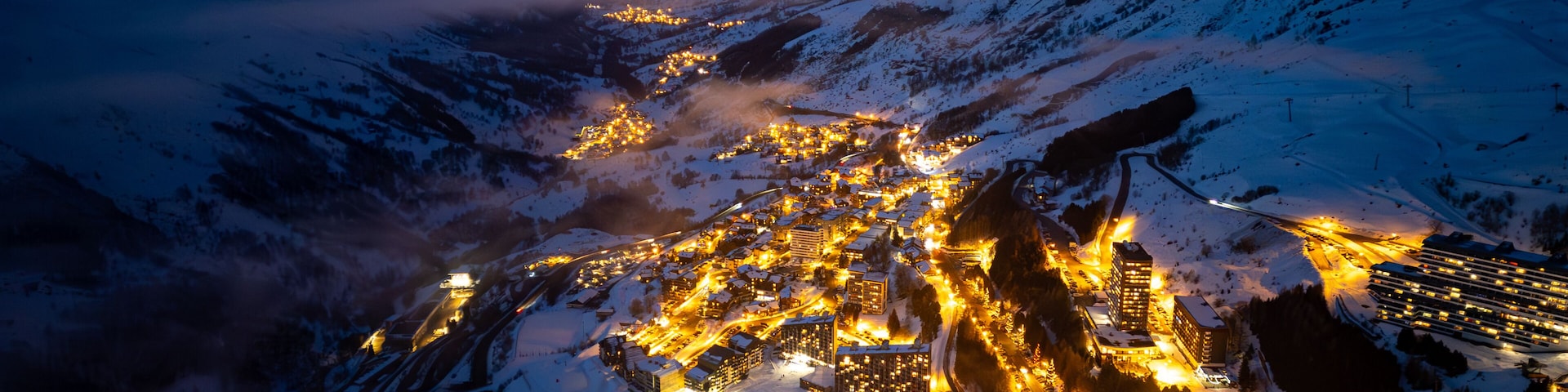 A snow-covered mountainous area with a town illuminated by artificial lights.