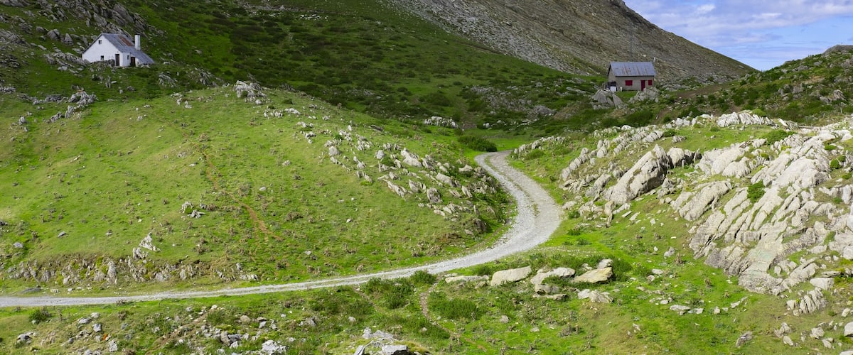 A winding mountain road, rocky terrain, and two white houses.