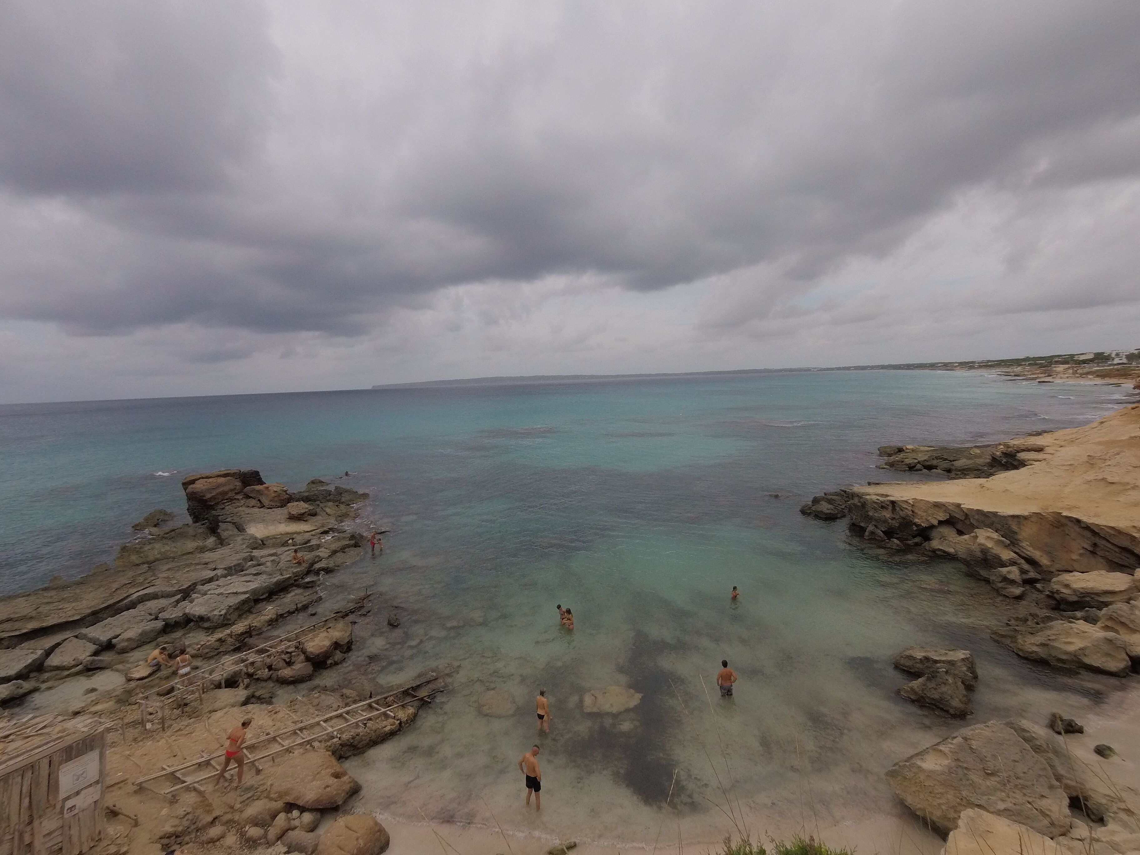 A rocky shoreline with clear turquoise water and overcast skies.