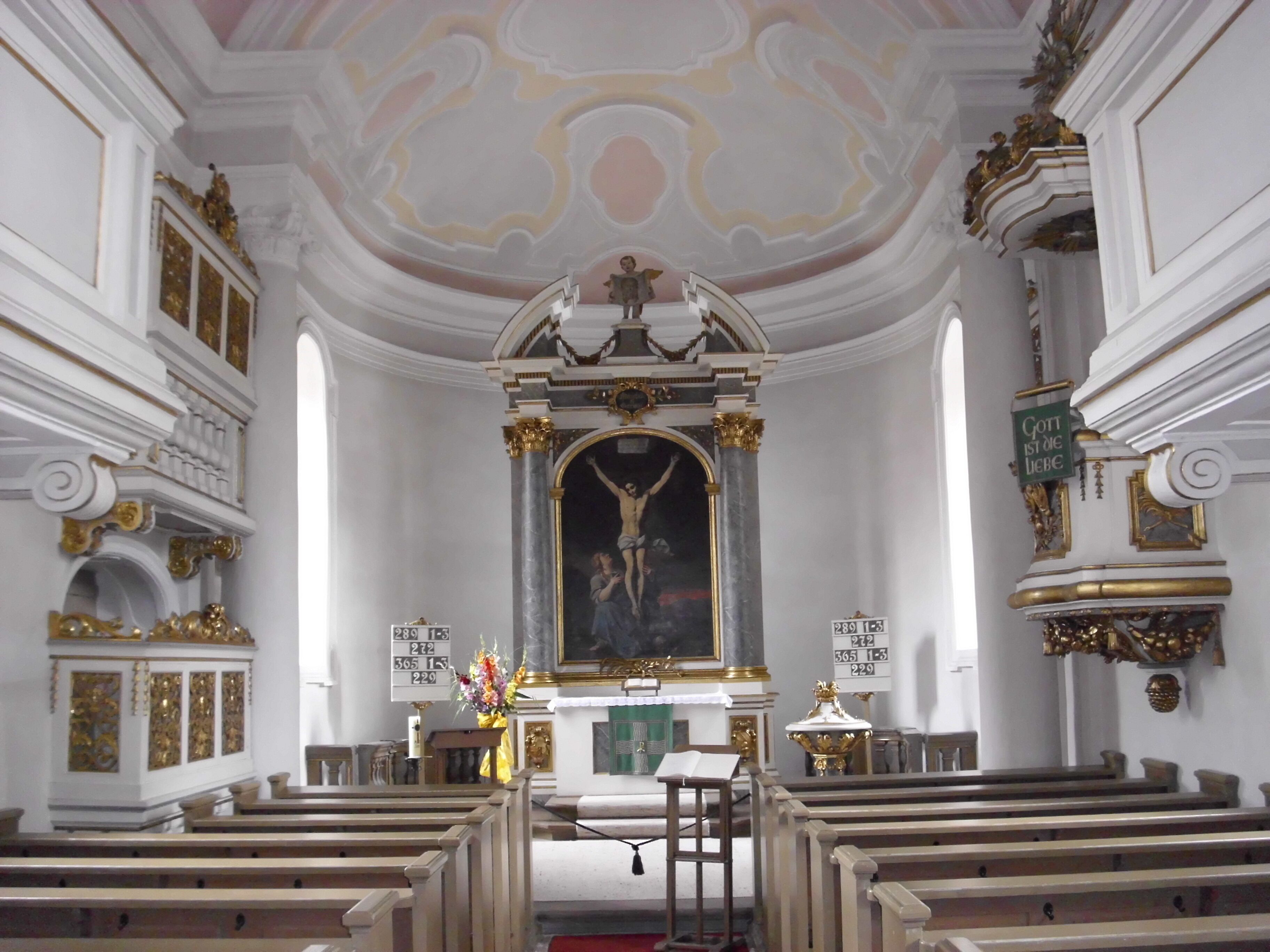 An ornate church interior with a crucifix, pews, and decorative columns.