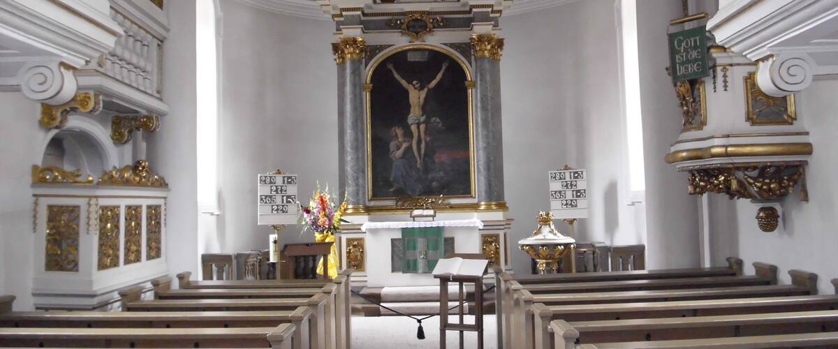 An ornate church interior with a crucifix, pews, and decorative columns.