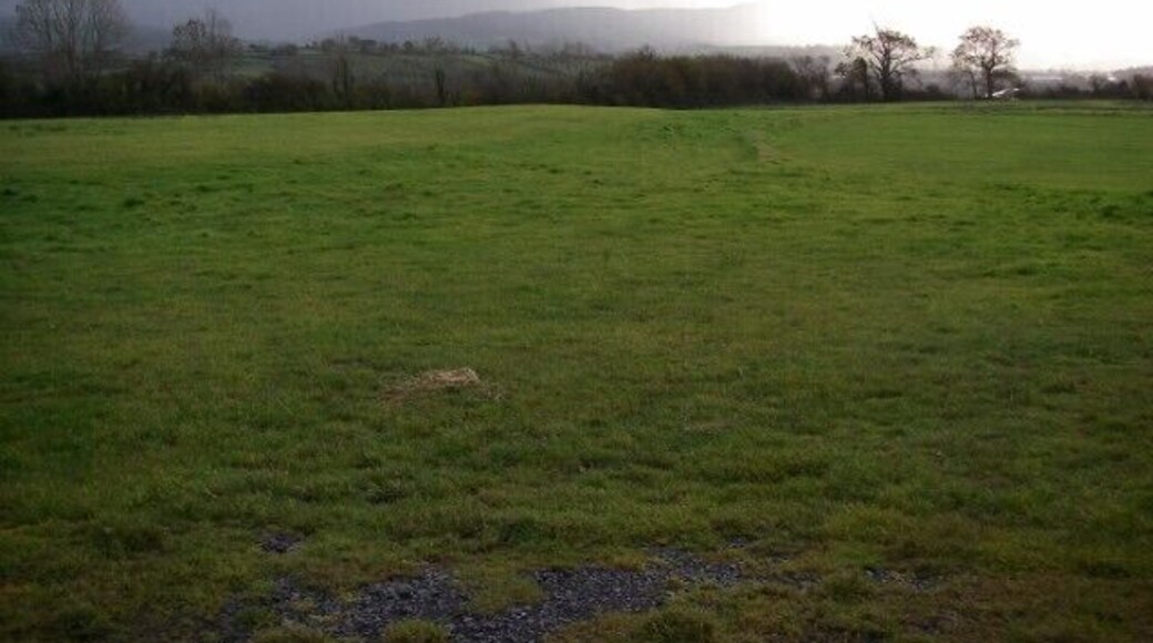 Heavy shower over Towy valley In the foreground, the subdued remains of an ancient settlement on the left and a modern cricket pitch on the right. In the background, the distant hills are progressively obscured by rain and hail.