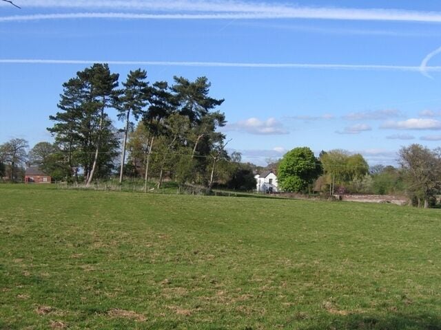A grassy field with trees and a white building in the distance.