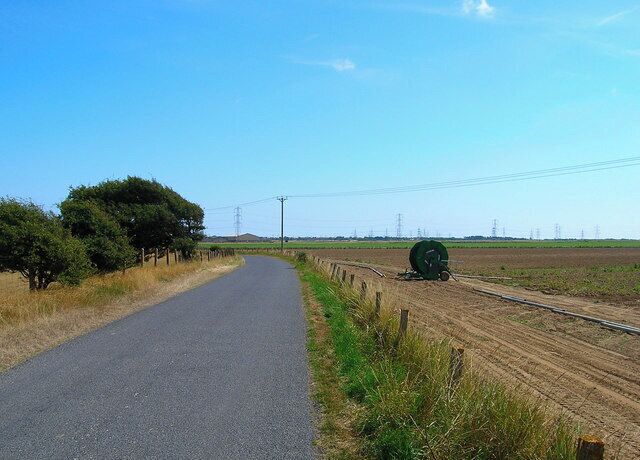 Midley Wall. Taken from near the entrance of Newland Farm. Once a sea wall formed to protect the now disappeared village of Midley and the newly inned fields to the north and east of Walland Marsh. You can see the drop in height on both sides of the lane though the former sea side of the wall is now at a greater height than the land that was once protected. Midley Wall runs from Westbrook Farm north to Wheelgate near Old Romney Farm. Many of the former embankments and walls provided useful methods of communication and consequently have become lanes many of which dot the Romeny Marsh landscape. The apparatus to the right is a crop sprayer linked to sewer near Horsebones Bridge.