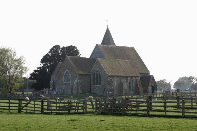 A church with a thatched roof and a steeple, surrounded by a wooden fence and green grass.