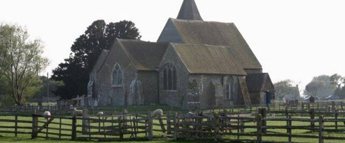 A church with a thatched roof and a steeple, surrounded by a wooden fence and green grass.