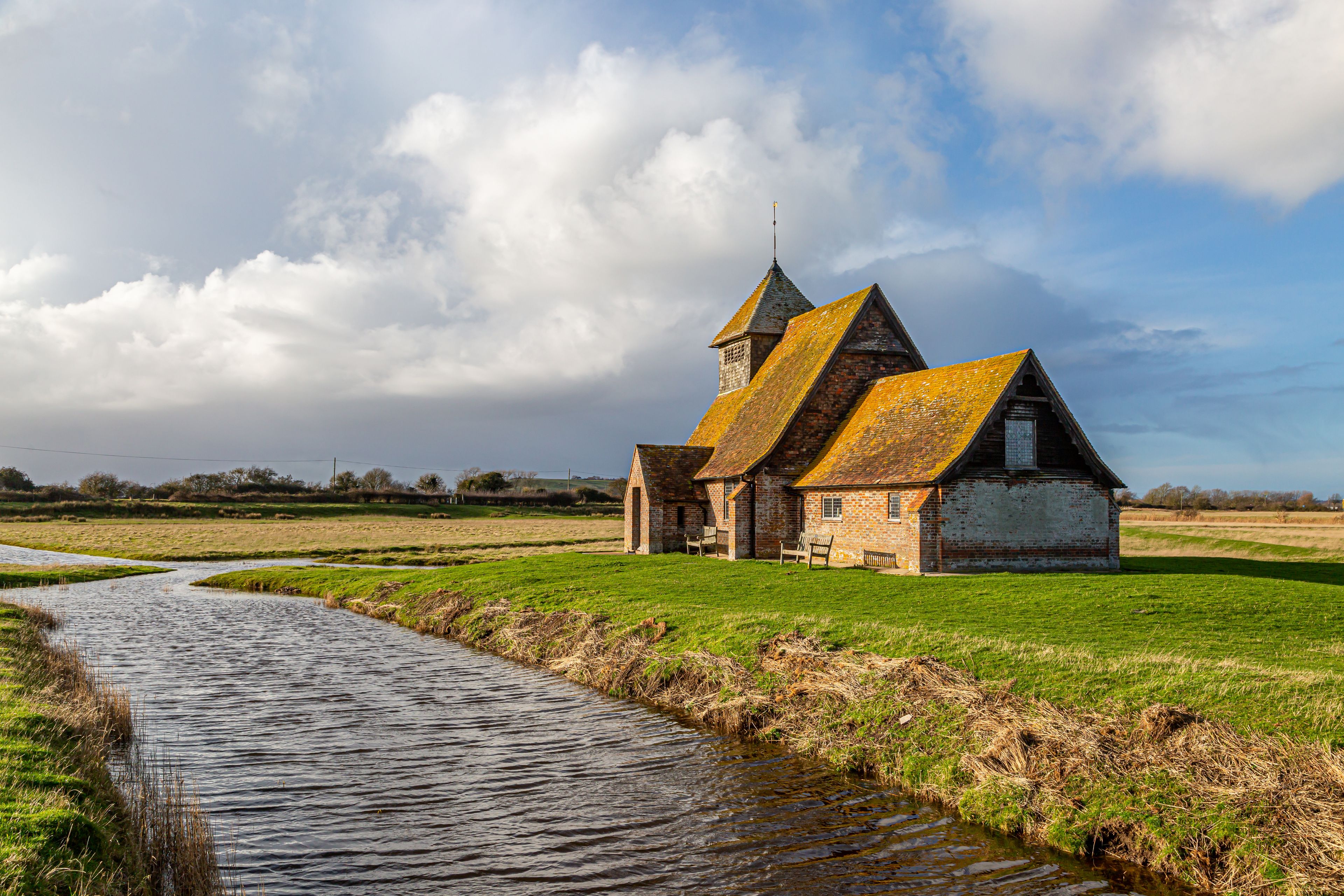 A traditional brick church with a steeply pitched roof and a tower, situated beside a narrow water channel.