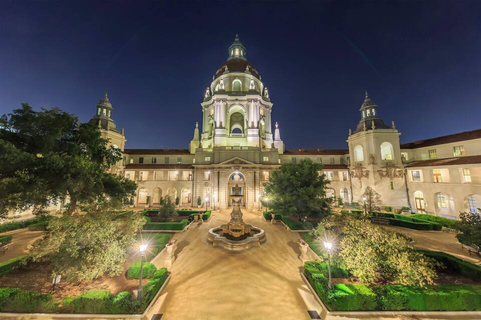 A grand building with a central dome and two towers, surrounded by well-manicured gardens and a fountain.