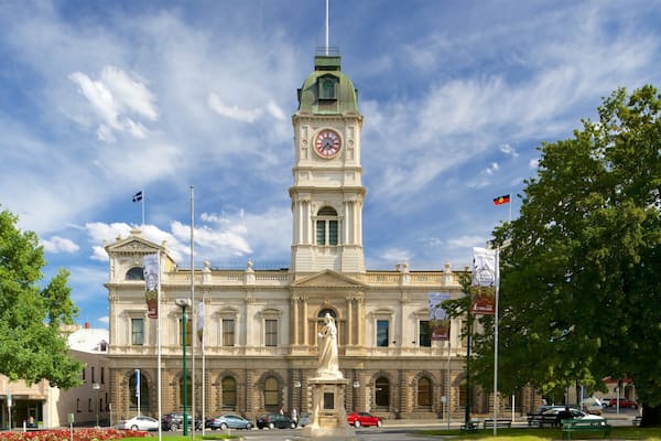 A historic building with a clock tower, a statue in front, and a flagpole with flags.