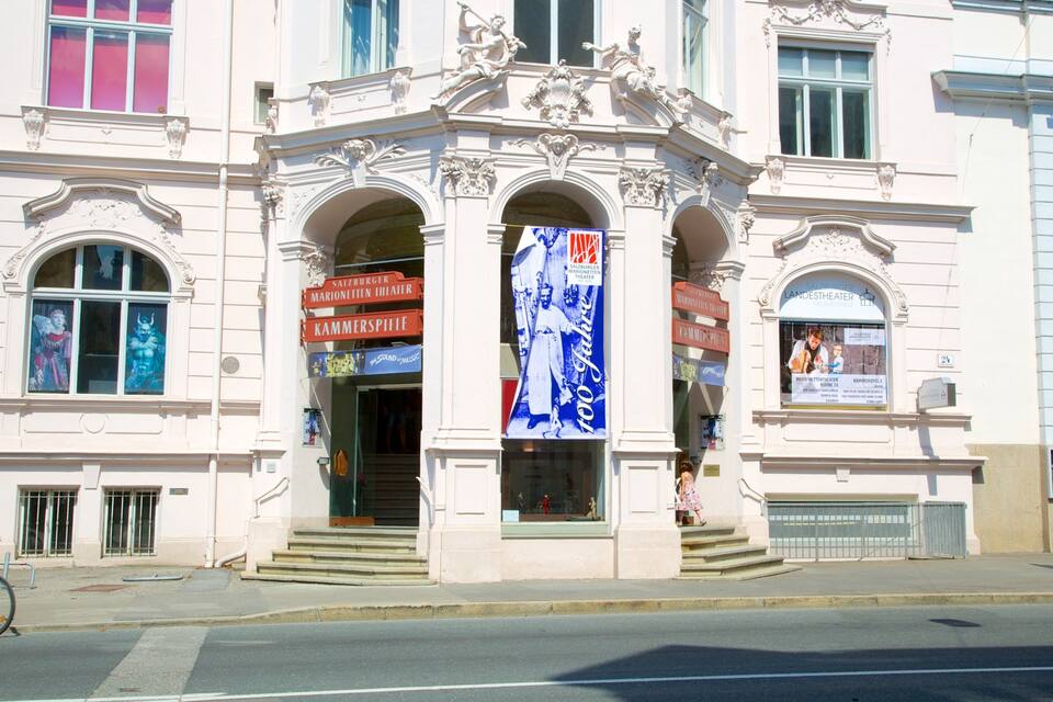 A classical building with ornate architecture, including columns and statues, and signs for the Salzburger Landtheater and Kammerspiel.