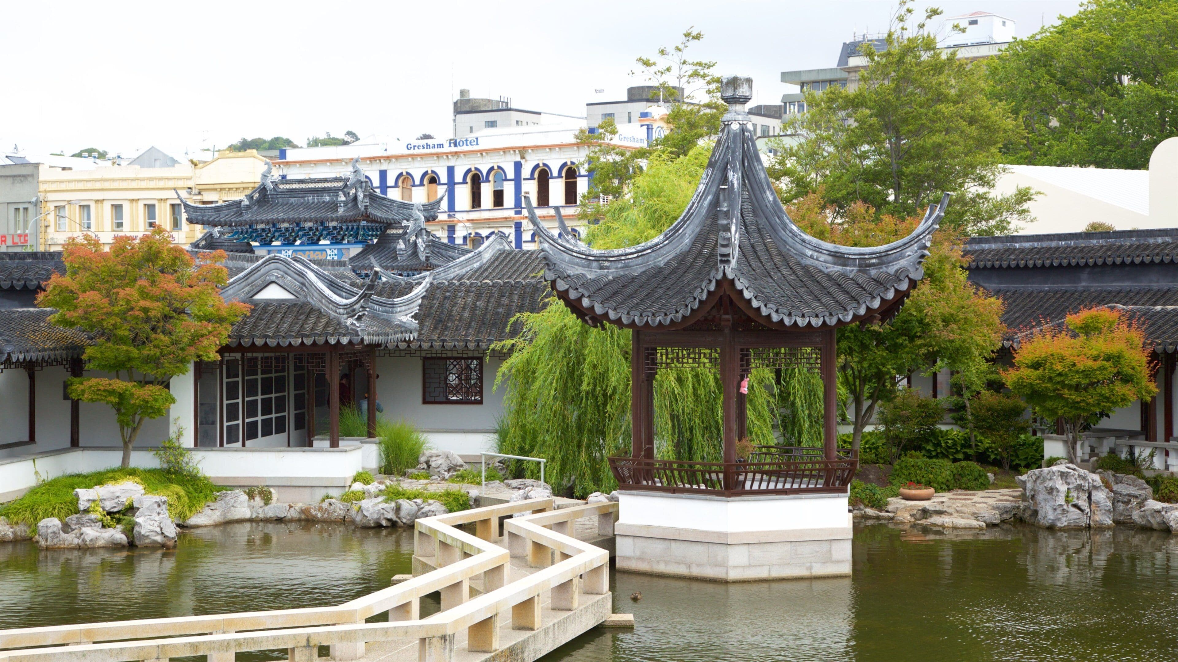 A traditional Chinese pavilion with a curved roof, a stone bridge, and a pond.