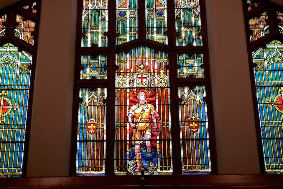 A stained glass window with a central figure and heraldic symbols.