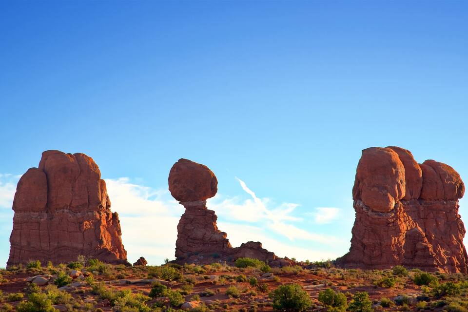 Drei markante rote Felsenformationen in einer Wüstenlandschaft unter blauem Himmel.