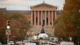 A large building with columns and banners, surrounded by trees and cars.