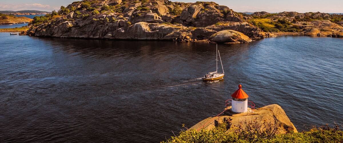 A rocky island with a lighthouse and a sailboat in the water.
