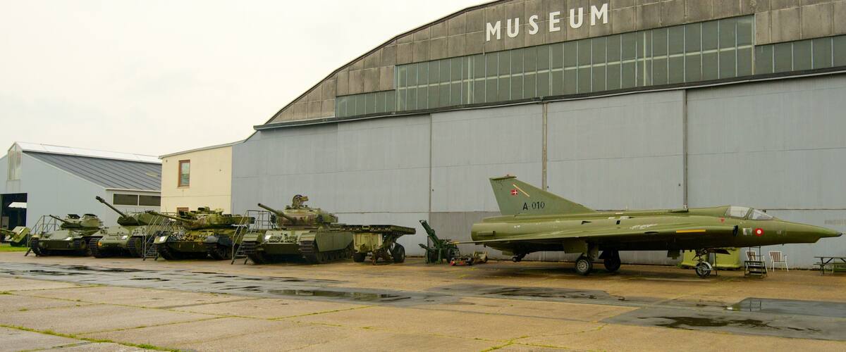A museum with a green fighter jet and several tanks in front.