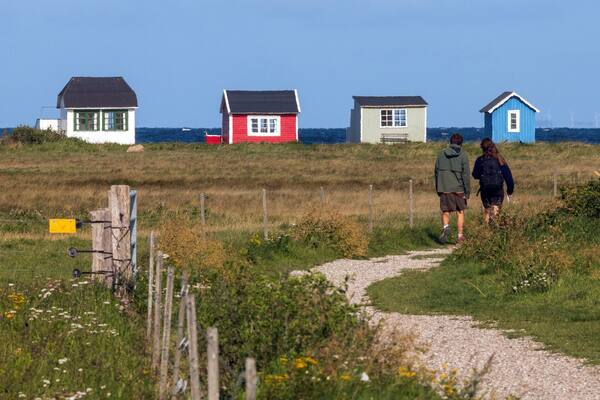 Young couple walking along the salt marsh to the colorful beach huts at Vesterstrand, Ærøskøbing, Ærø, Denmark