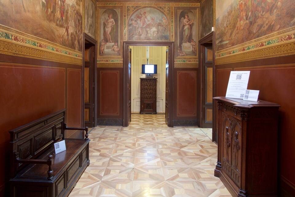 A grand hallway with ornate wood paneling, a tiled floor, and classical frescoes on the walls.