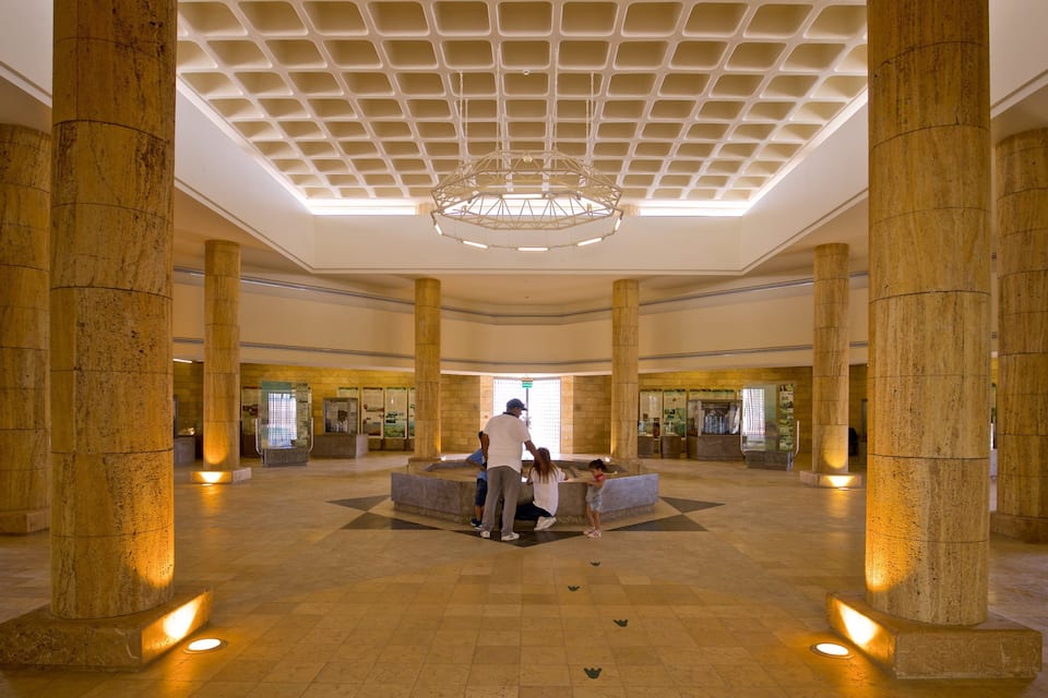A grand lobby with large stone columns, a geometric ceiling design, and a central seating area.