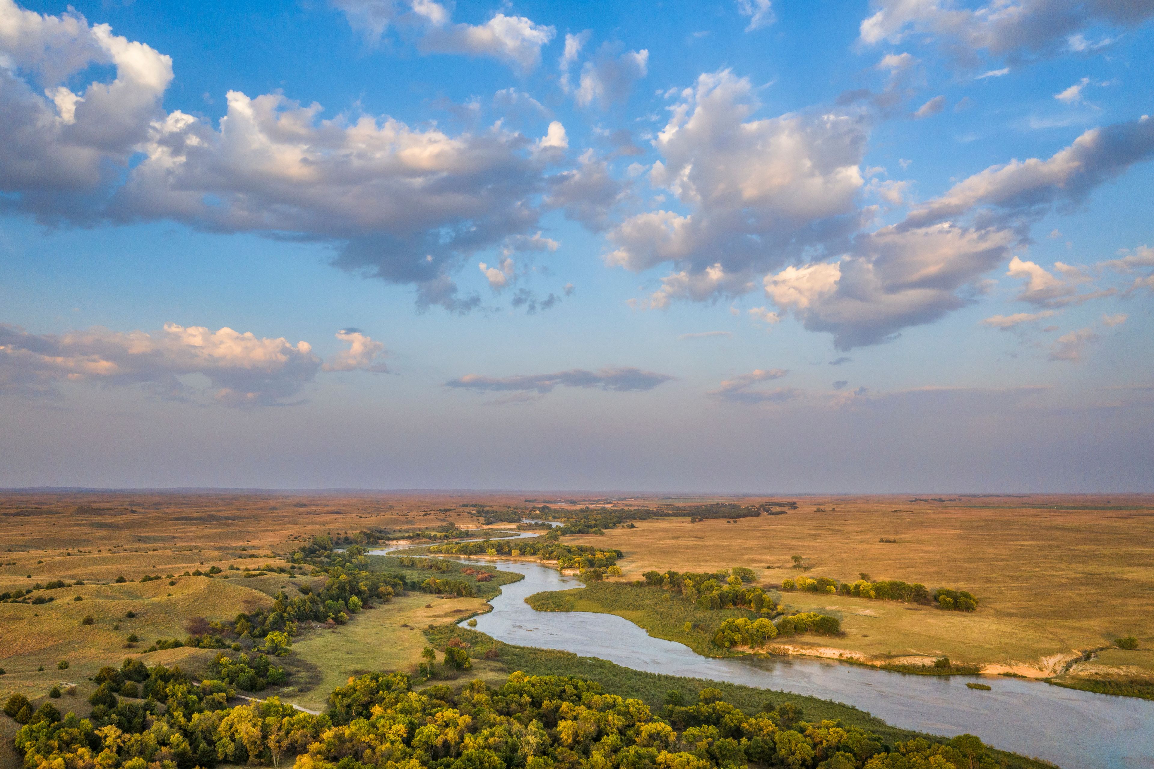 A river winding through a landscape with scattered trees and open fields under a partly cloudy sky.