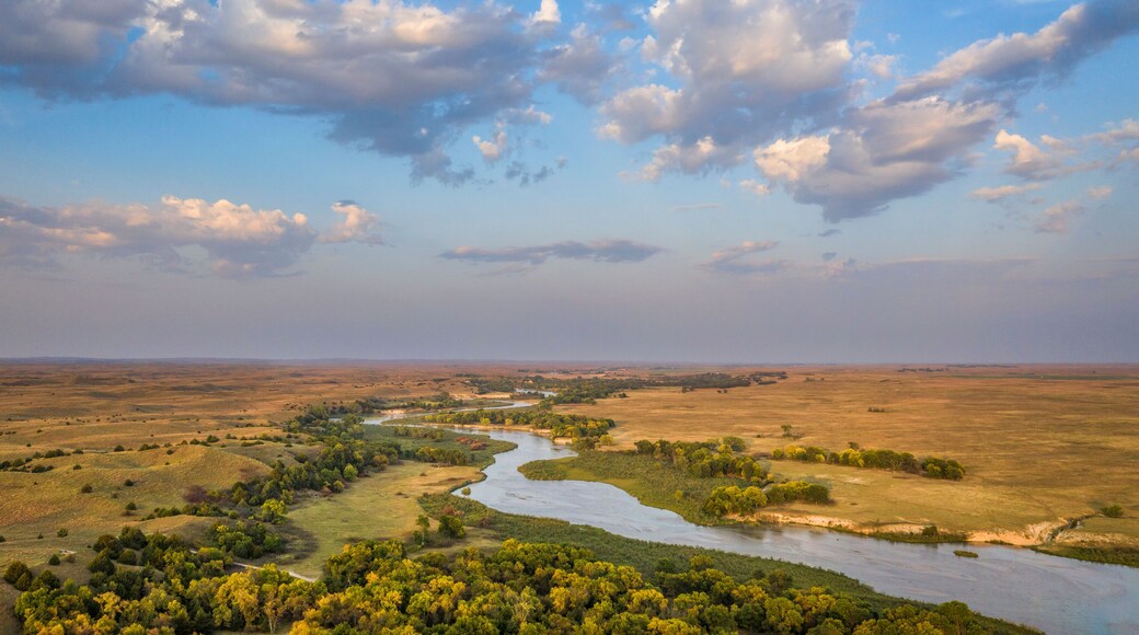 A river winding through a landscape with scattered trees and open fields under a partly cloudy sky.
