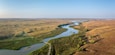Een rivier slingert door een landschap met stukken groen en dor gras.