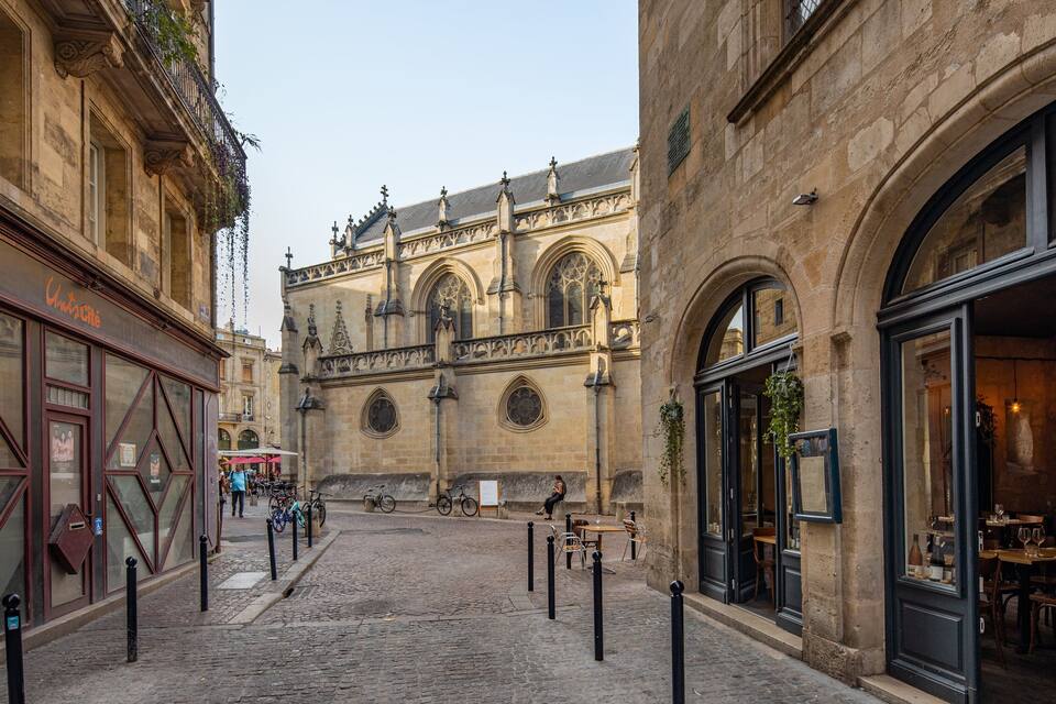 A cobblestone street with historic buildings, a café, and a church in the background.