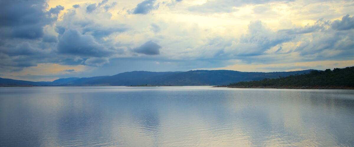 A calm lake with mountains in the background and a cloudy sky.