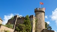 Un château de pierre historique, surmonté d’un drapeau, entouré d’arbres et se dressant sous un ciel bleu clair.