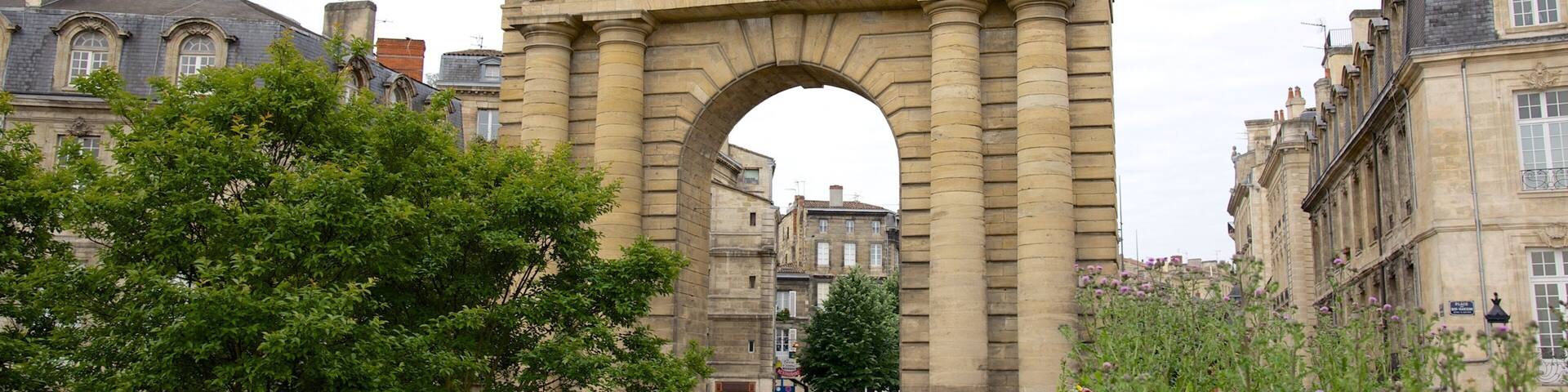 An archway with classical architecture, surrounded by lush greenery and historic buildings.
