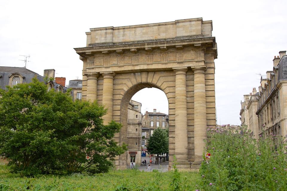 An archway with classical architecture, surrounded by lush greenery and historic buildings.