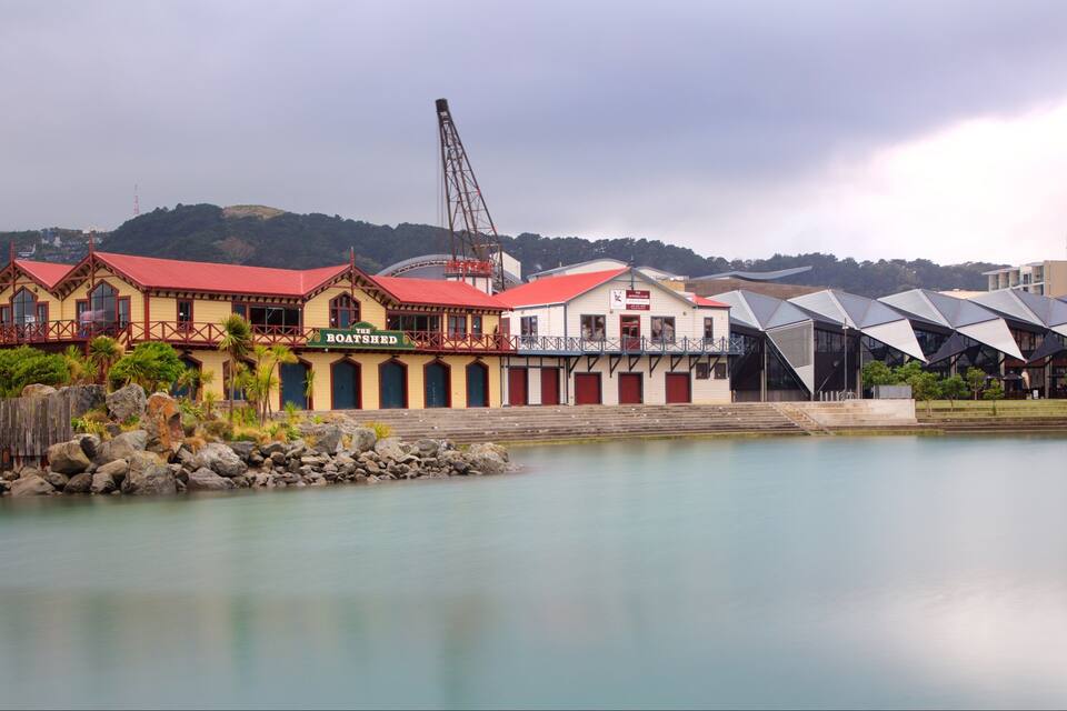 A waterfront with a boathouse, a crane, and modern buildings.