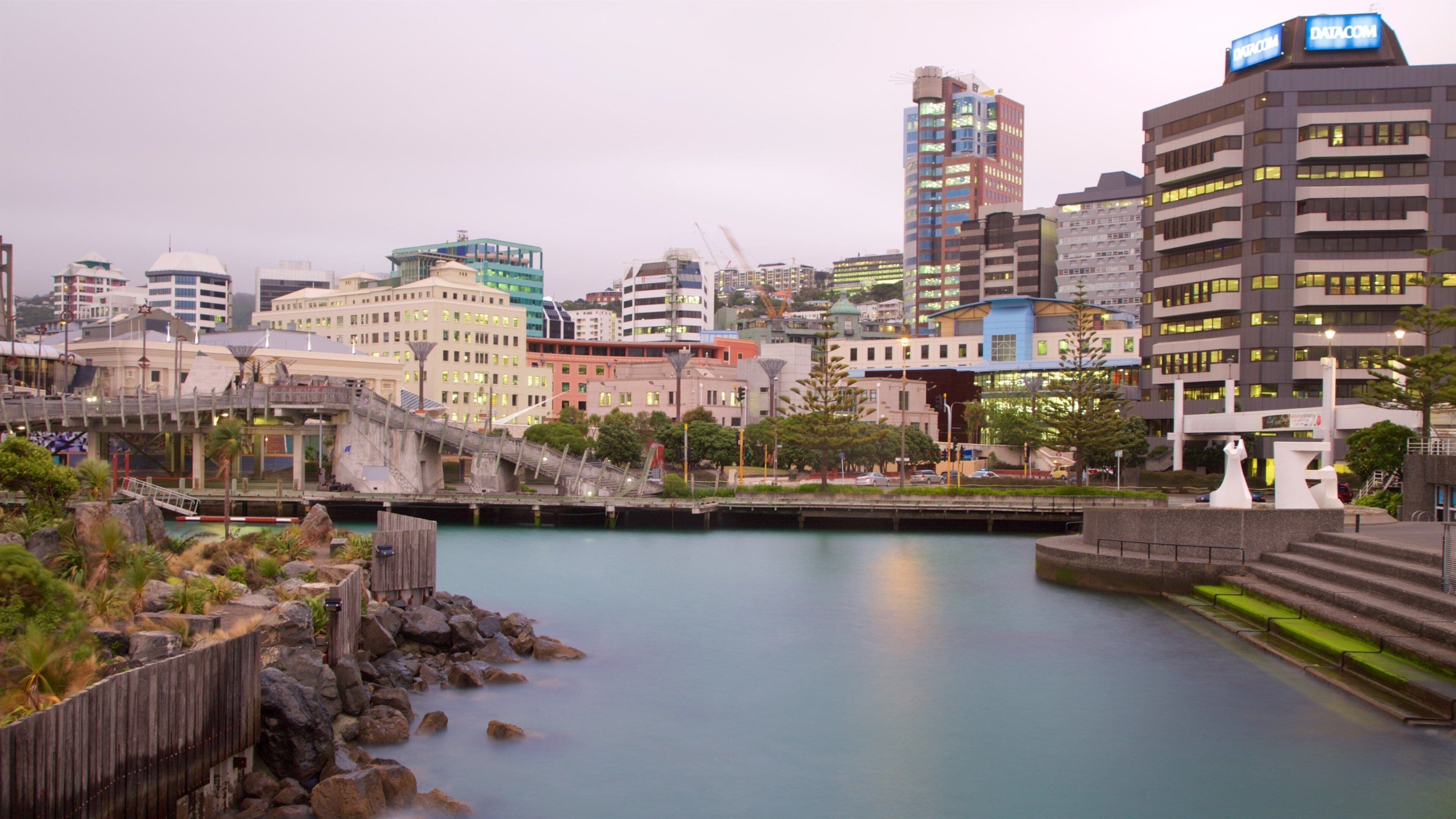 A cityscape with a river, modern buildings, and a wooden bridge.