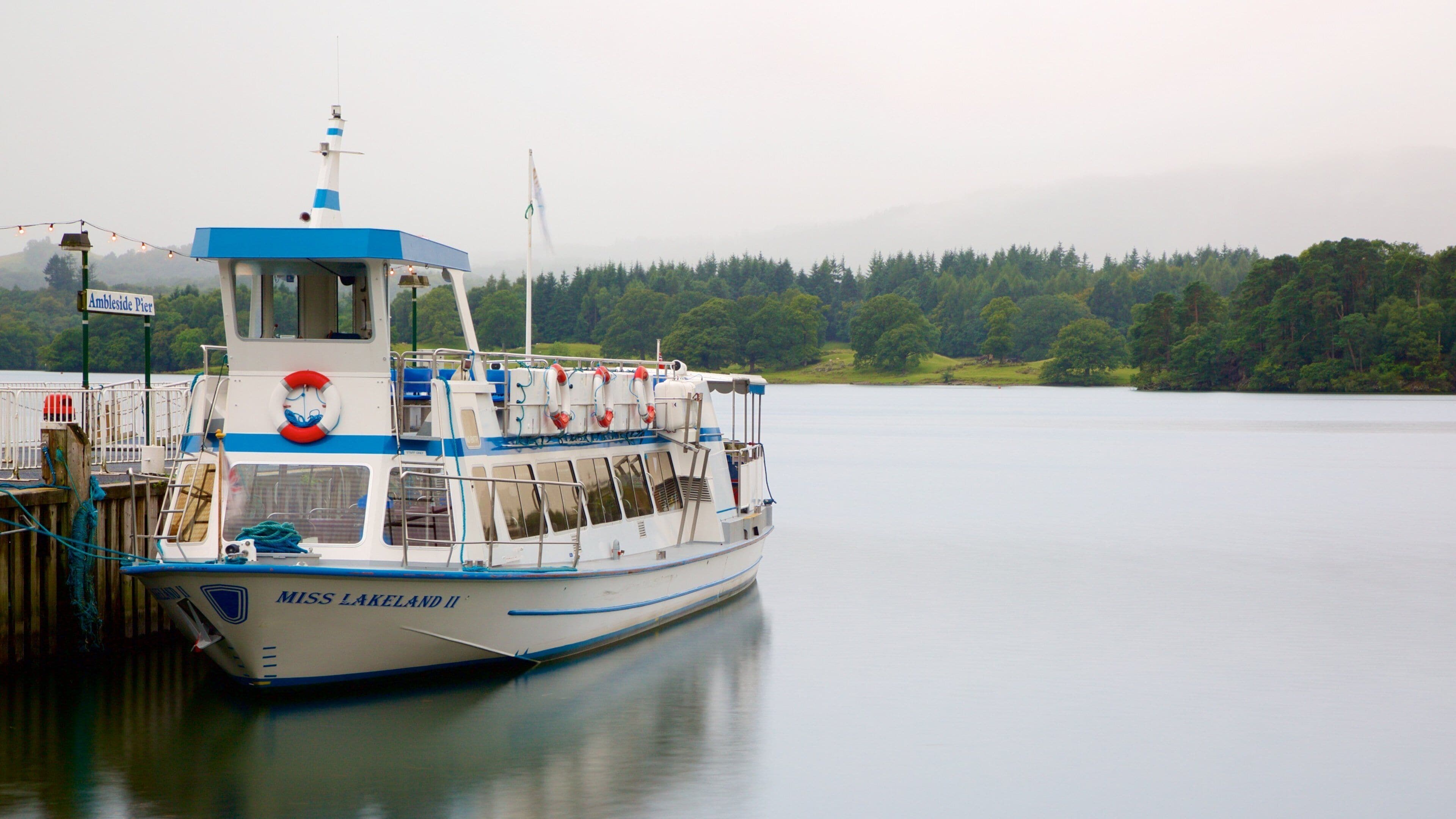 A boat named Miss Lakeland II docked at a pier with a forested shoreline in the background.