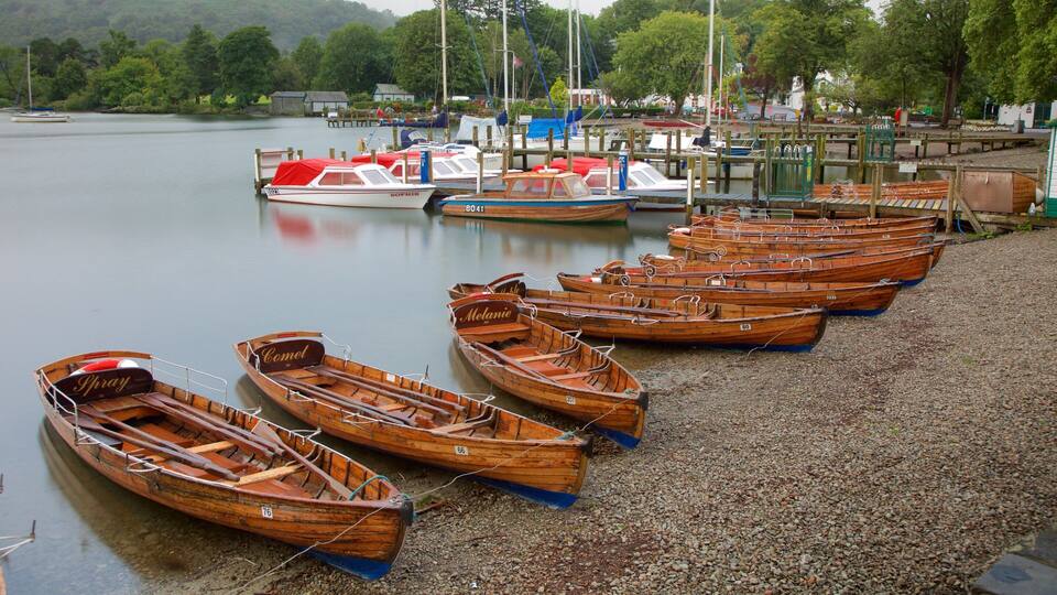 A row of wooden rowboats lined up on a gravel dock by a calm lake.