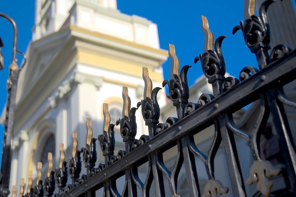 Ornate black metal railings with intricate designs, a clear blue sky, and a white building with yellow accents in the background.