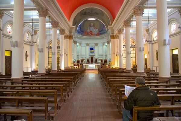 Ein Kircheninneres mit Reihen hölzerner Kirchenbänke, weißen Säulen und einem zentralen Altar.