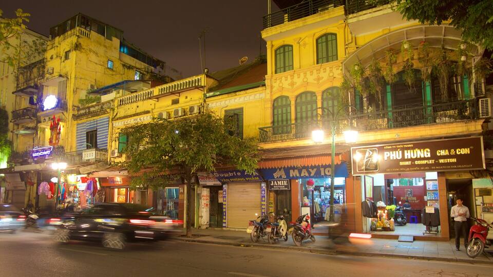 Calle nocturna con edificios, tiendas y motocicletas estacionadas.