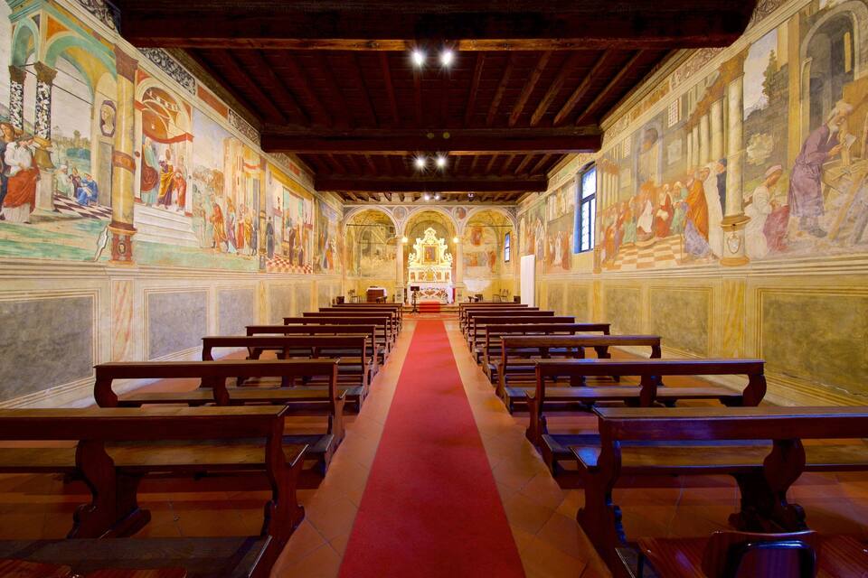 Interior d'una església amb pews de fusta, una catifa vermella i frescos a les parets.